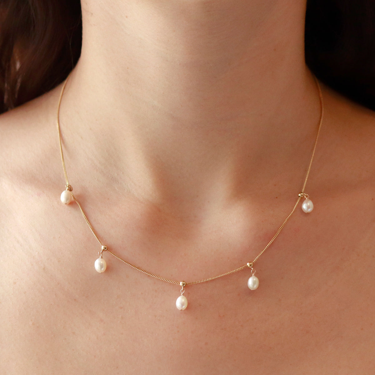 Model wearing a delicate adjustable white pearl necklace, showcasing its elegant design.
