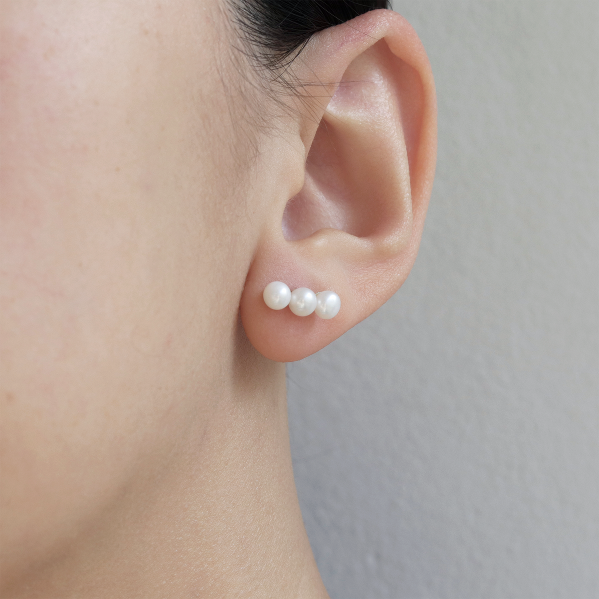 Small triple pearl studs worn on model, offering a refined and elegant look for any occasion.